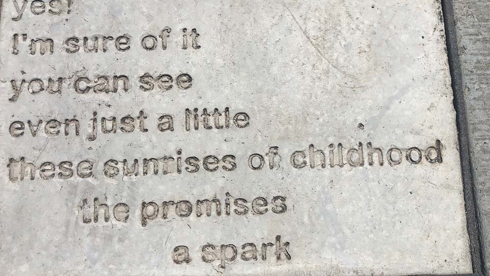 Sidewalk Poetry closeup with the words "yes! I'm sure of it. you can see. even ust a little. these surises of childhood. the promises. a spark" set in concrete