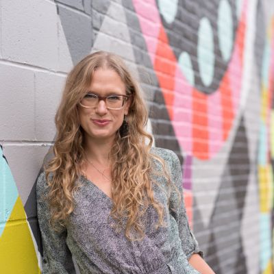 Kim Carlio standing against a mural wall smiling