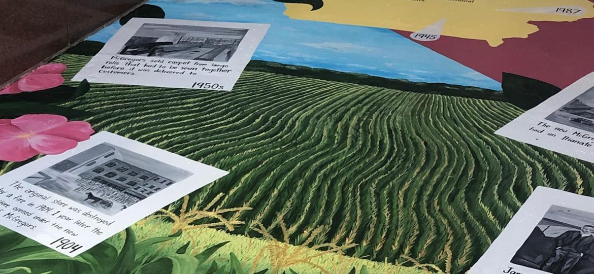 A closeup of the McGregor's mural with farm fields and dated painted photos of historical moments