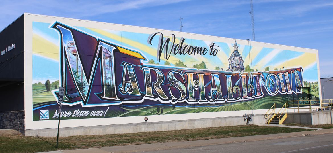 A full exterior wall mural that reads 'Welcome to' in script above large letters that read 'MARSHALLTOWN' with images of the city inside each letter