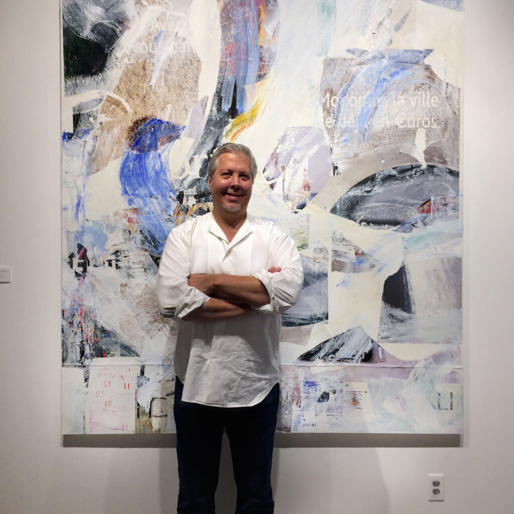 a portrait of Stephen smiling with arms crossed in front of a colorful abstract painting
